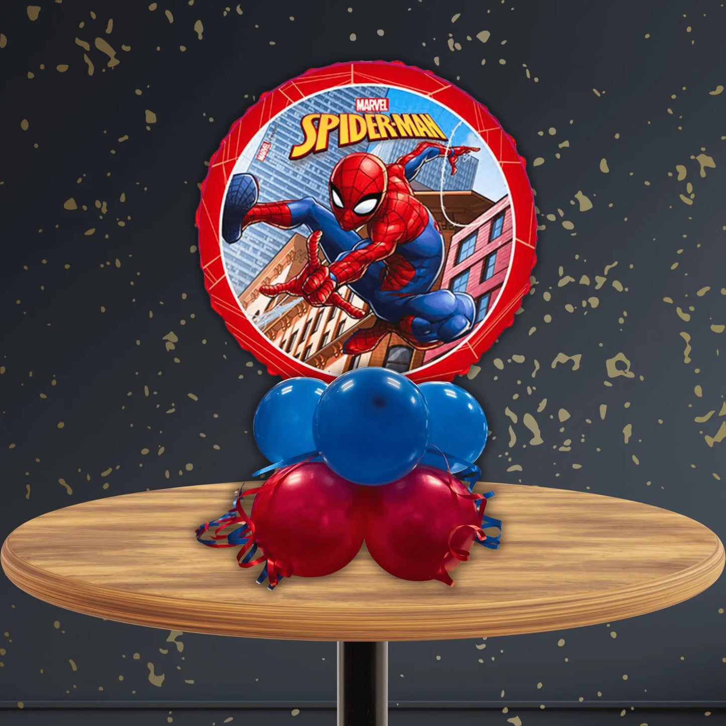 18-inch Spider-Man Air-Filled Birthday Balloon Table Stack featuring a round foil balloon with Spider-Man swinging through city buildings, supported by alternating red and blue balloon base, displayed on wooden table against dark background
